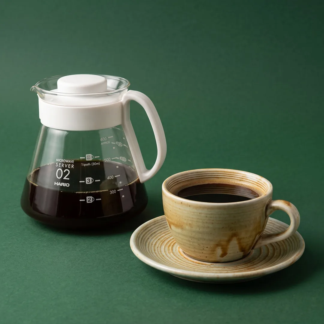 V60 pour over brewing into a glass carafe beside a filled cup