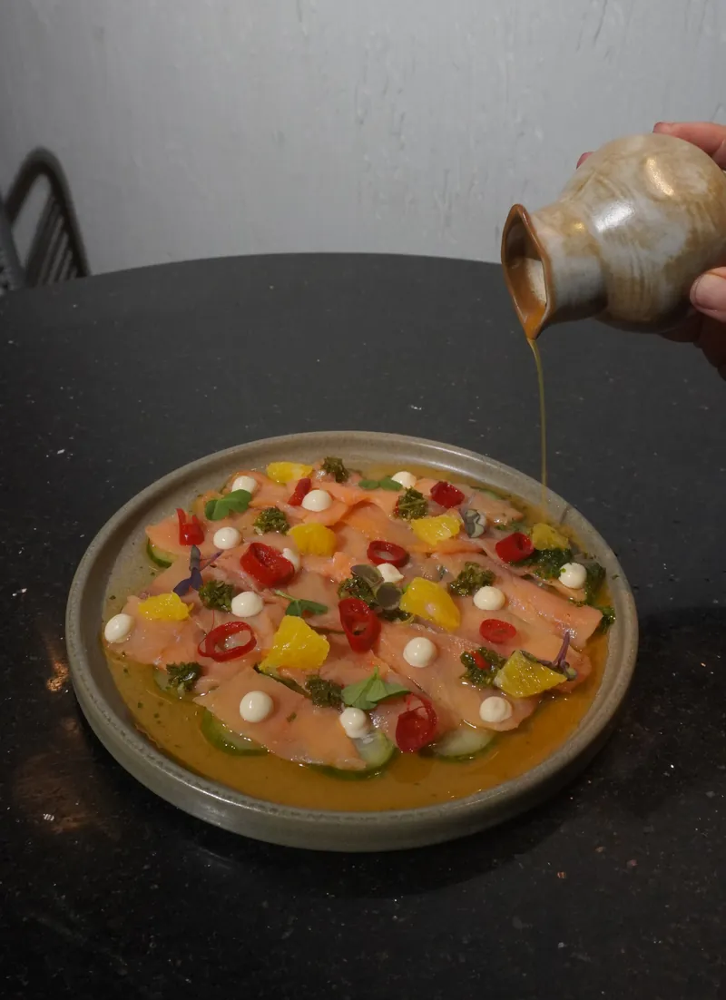 Salmon crudo with citrus, cherry tomato and a dressing poured at the table
