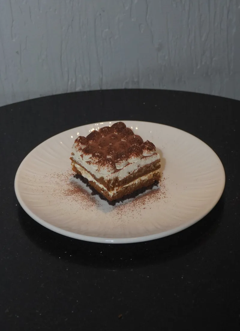 Classic tiramisu dusted with cocoa on a pale ceramic plate